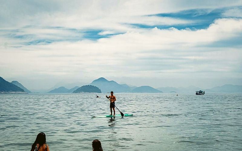 Uma pessoa no mar de copacabana praticando Stand Up Paddle