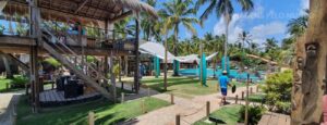 Beach Club em Maceió: Piscina e lounge do Milagres dos Toque com muitas palmeiras ao fundo e um céu azul com sol bem forte