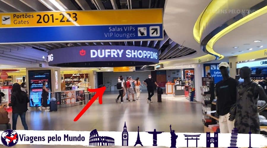 Aeroporto de Guarulhos. Duty Free e corredor de passageiros passando.