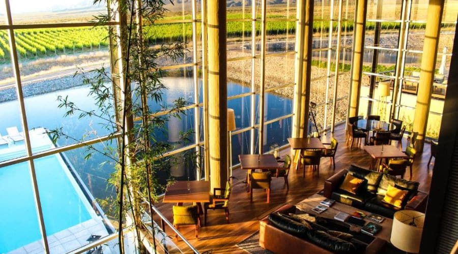 Vale de Uco Resort: sala de Estar Interna com vista para a Piscina, uma sala de estar espaçosa com janelas grandes, mobiliário de madeira e confortáveis assentos, olhando para uma piscina externa e vinhedos ao fundo, combinando luxo e natureza