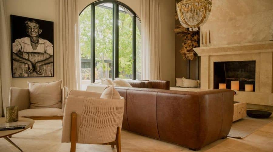 Sala de estar sofisticada da Suíte 
 do Suzana Balbo com móveis modernos e uma grande janela arqueada que oferece uma vista para o jardim. A decoração inclui uma lareira, um lustre pendente e uma obra de arte em preto e branco na parede, criando um ambiente aconchegante e estiloso.