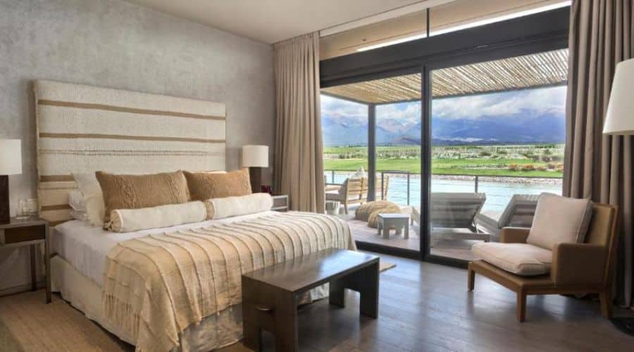The Vines Resort Mendoza: suíte com vista panorâmica. A suíte tem uma grande janela de vidro que oferece uma visão ampla e desobstruída das montanhas e do vinhedo, mobiliada elegantemente para garantir conforto e uma estadia prazerosa.
