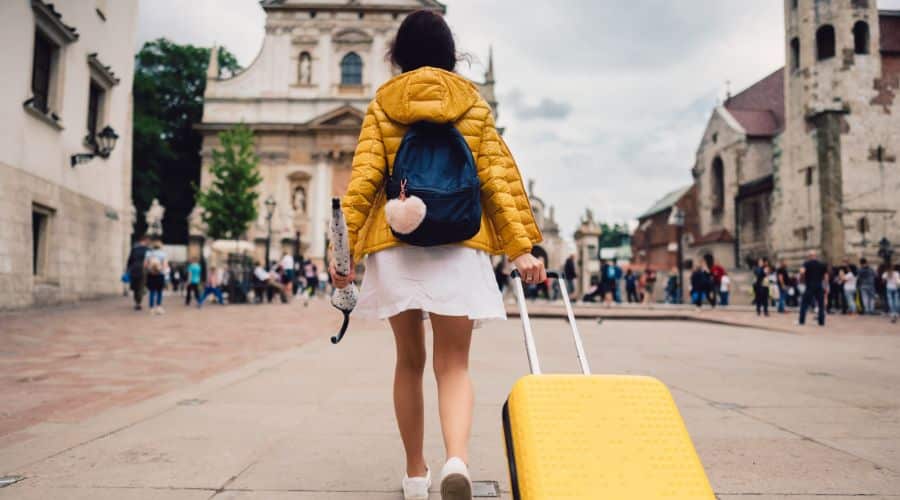 Real Seguro Viagem é confiável! Mulher com sua mala amarela caminhando para o hotel na cidade