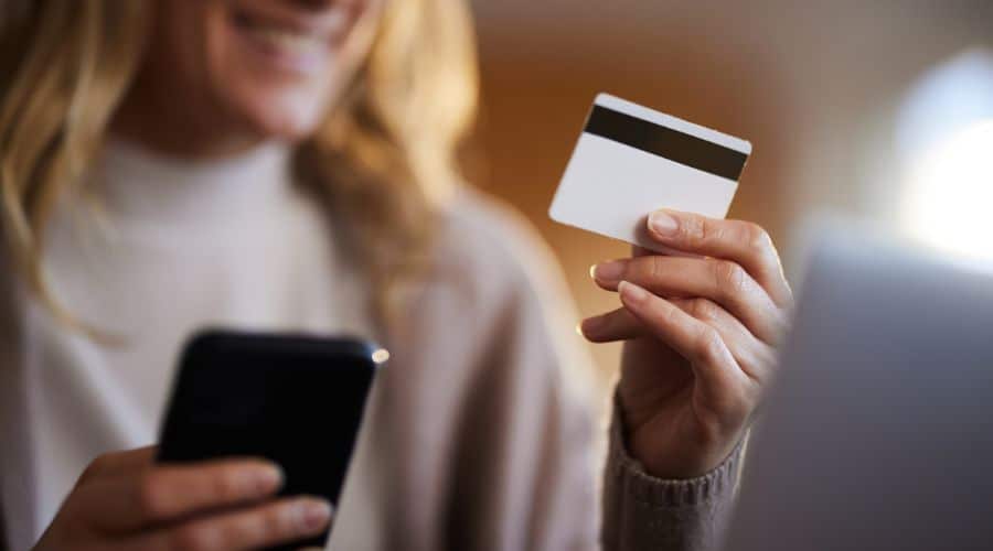 Comprando chip de internet para Orlando: Mulher segurando o celular em uma mão e o cartão de crédito na outra mão