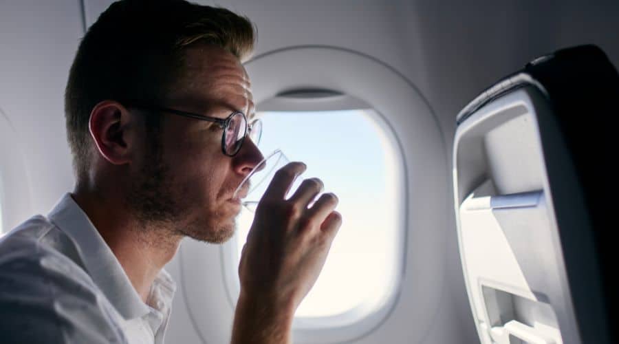 Homem sentado na poltrona da janela do avião e tomando um copo de água