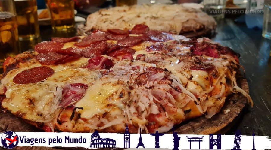 Duas pizzas grandes em cima da mesa com queijo escorrendo