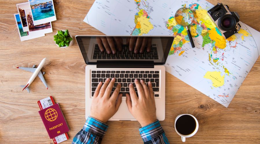 Pesquisando hospedagens mais baratas. Notebook aberto e passaporte ao lado com café.