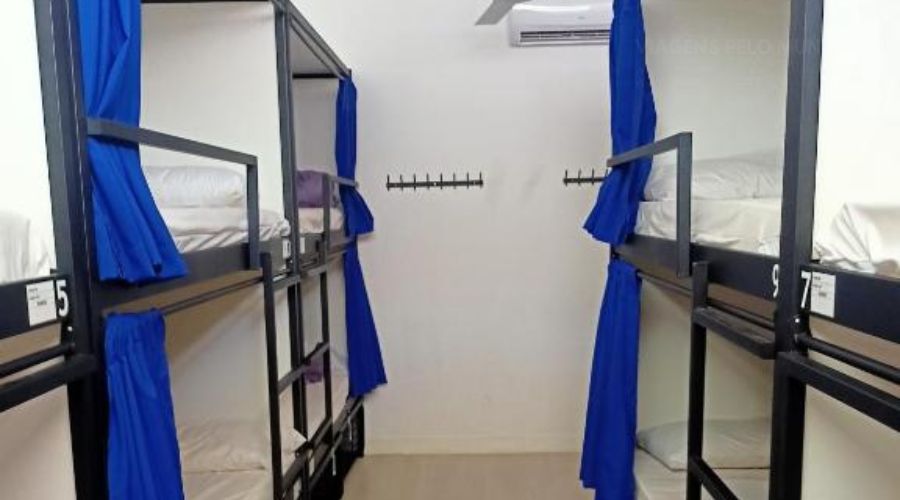 Quarto com beliches de ferro com cortinas para dar privacidade.