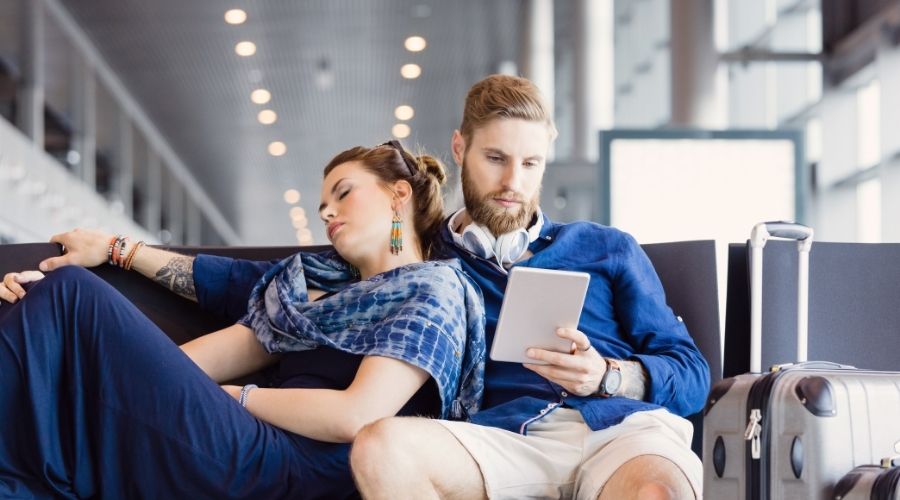 Casal aguarando no banco do aeroporto seu voo que está atrasado.